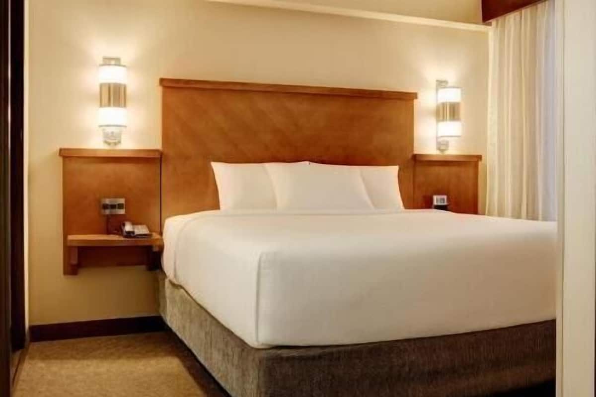 A hotel room with a large bed, wooden headboard, bedside tables, and wall-mounted lights.