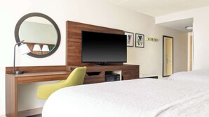 A hotel room with a bed, a desk with a television, a mirror, and a chair.