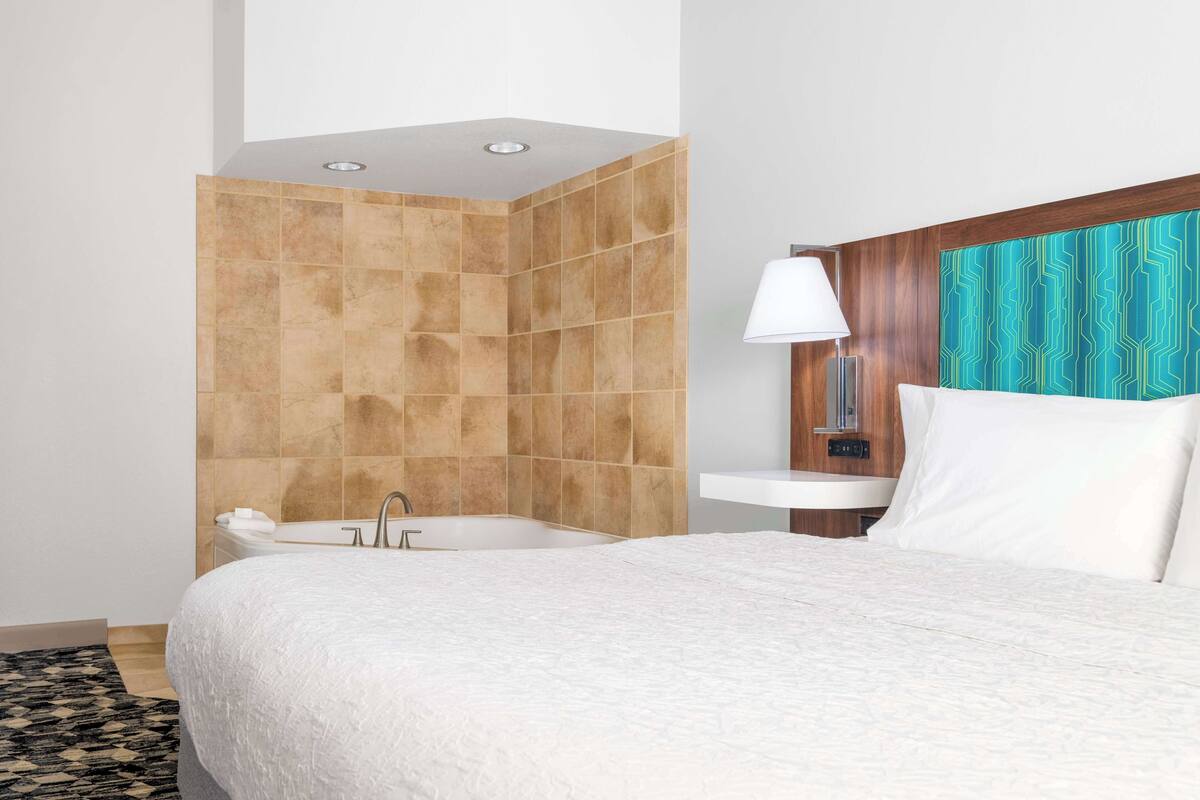 Quarto de hotel com uma cama grande, banheira, pia e chuveiro.