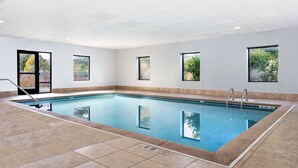 An indoor swimming pool with clear water, tiled floor, and windows offering views of greenery.