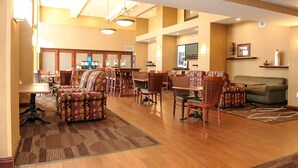 A spacious lobby with multiple seating areas, a coffee station, and a television mounted on the wall.