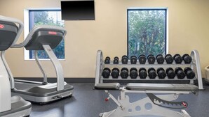 A gym with treadmills, a dumbbell rack, and a TV mounted on the wall.
