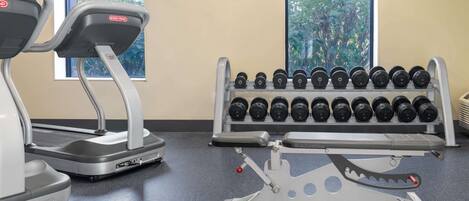 Un gimnasio con cintas de correr, un soporte para mancuernas y un televisor montado en la pared.