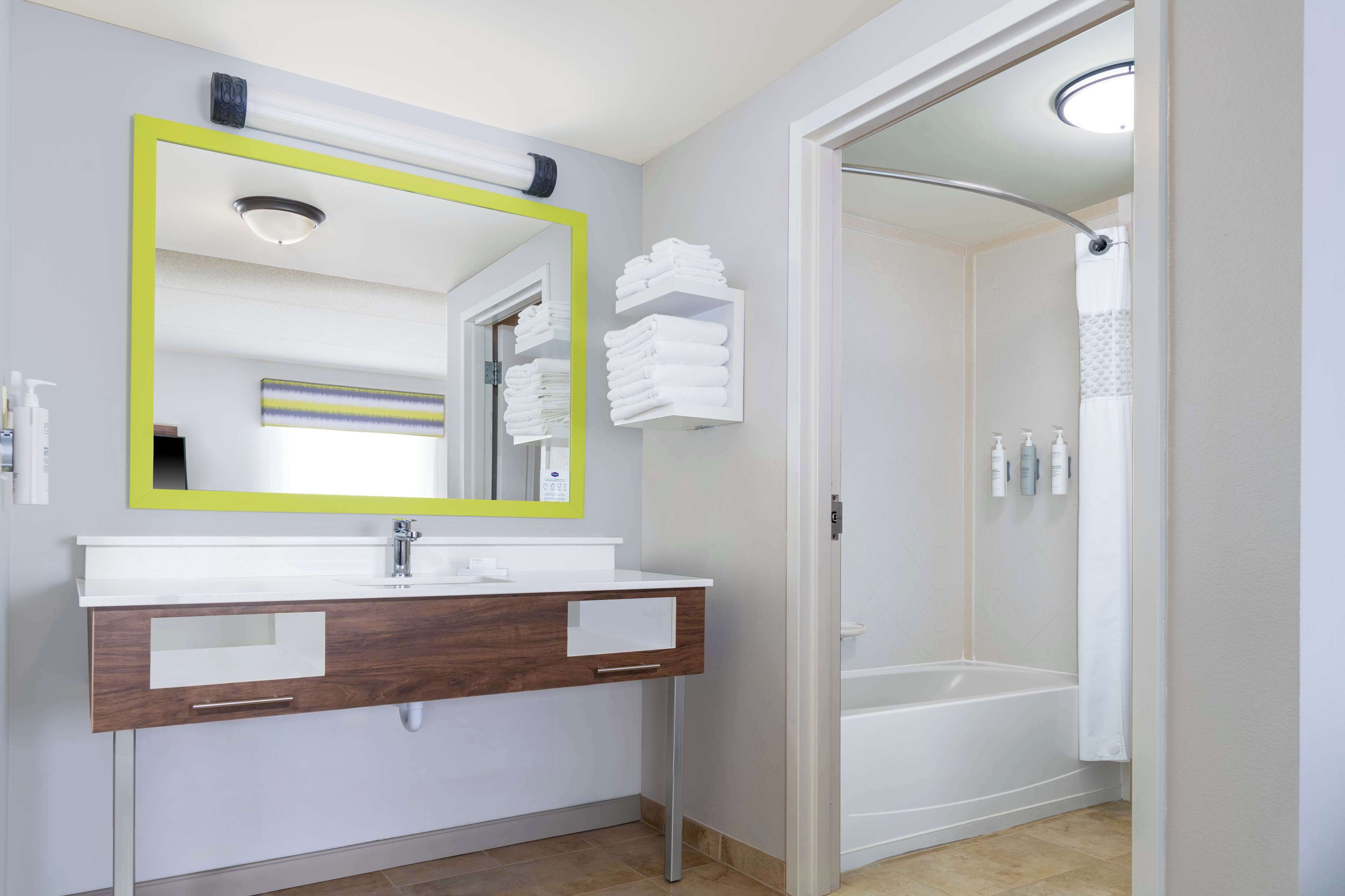 Un baño moderno con un tocador blanco, un espejo grande con marco amarillo y una zona de ducha.