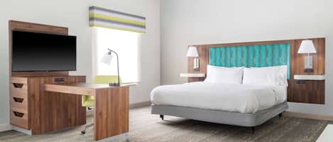 Habitación de hotel con cama, escritorio, televisor de pantalla plana, lámpara y ventana con cortinas.