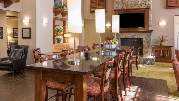 A spacious living room with a large wooden dining table, multiple chairs, a stone fireplace, and a flat-screen TV mounted on the wall. - Hampton Inn & Suites Florence-North-I-95 (Florence)