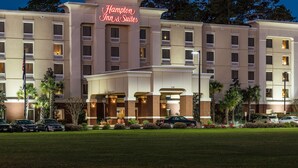 A Hampton Inn & Suites hotel with a well-lit entrance, multiple floors, and a parking area.