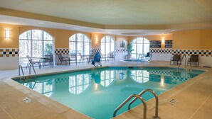 An indoor swimming pool with clear water, surrounded by a checkered wall pattern, and equipped with multiple seating areas and a lifeguard station.