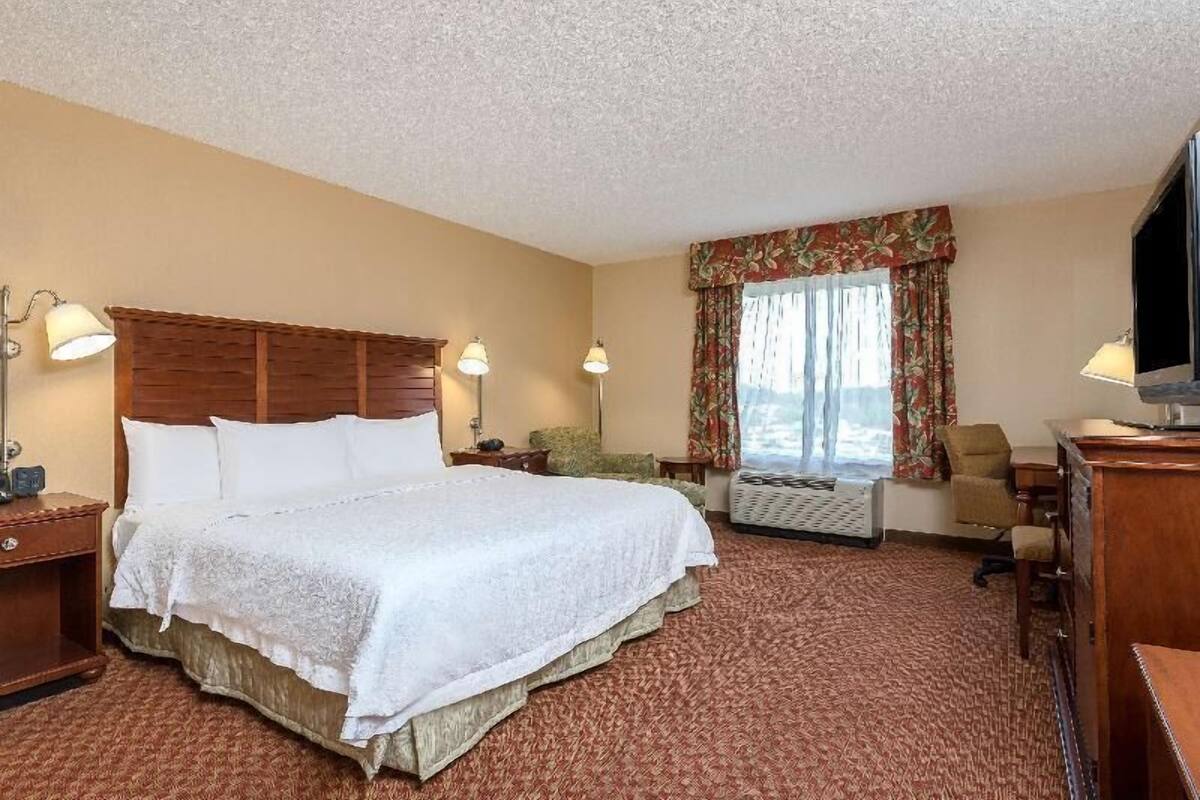 Una habitación de hotel con una cama grande, dos lámparas de noche, un escritorio con silla, un televisor y una ventana con cortinas.