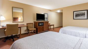 A hotel room with two beds, a desk with a chair, a television, and a framed picture on the wall.
