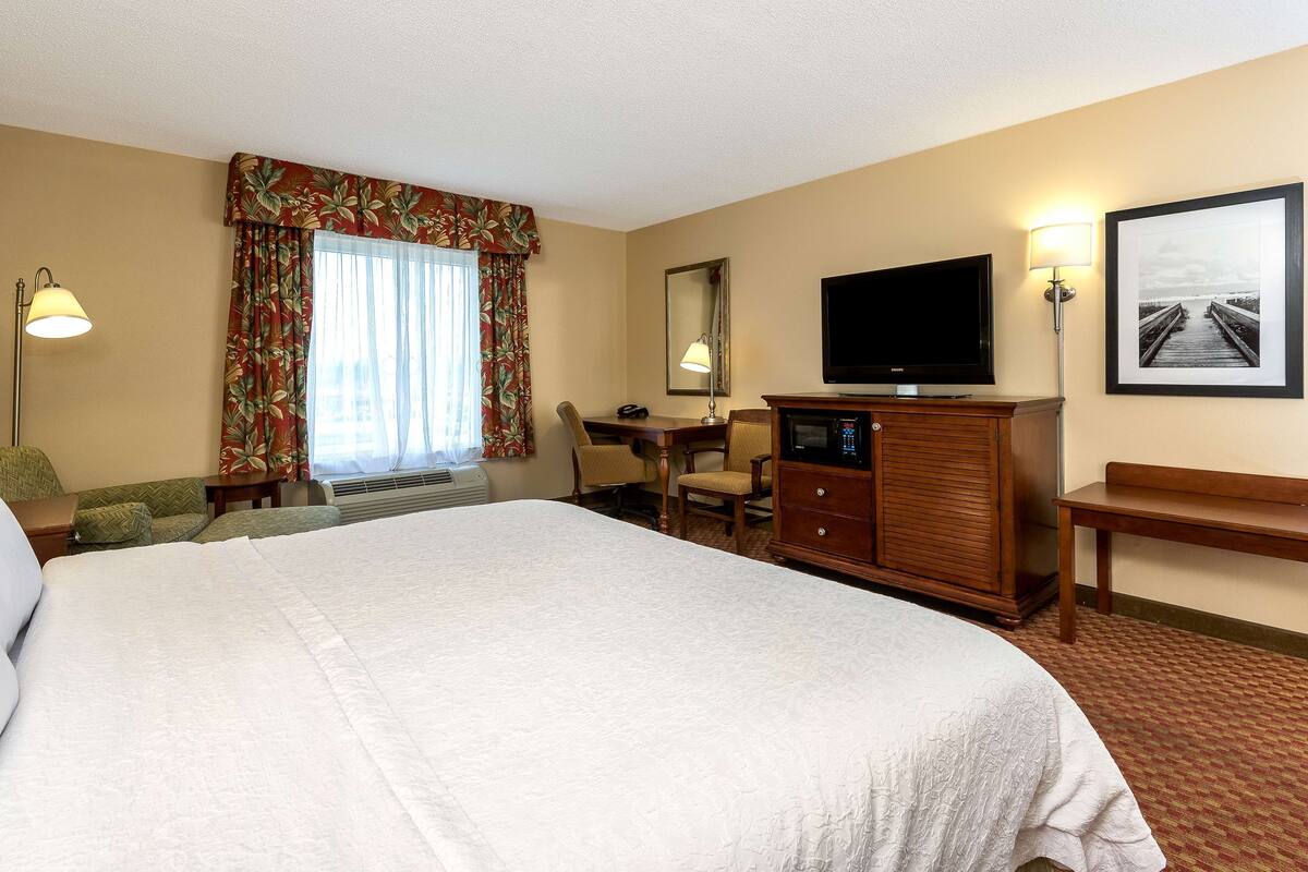 Habitación de hotel con una cama grande, un escritorio con computadora, televisor y una silla.