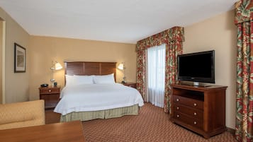 A hotel room with a large bed, a TV on a wooden stand, a desk, and a chair.