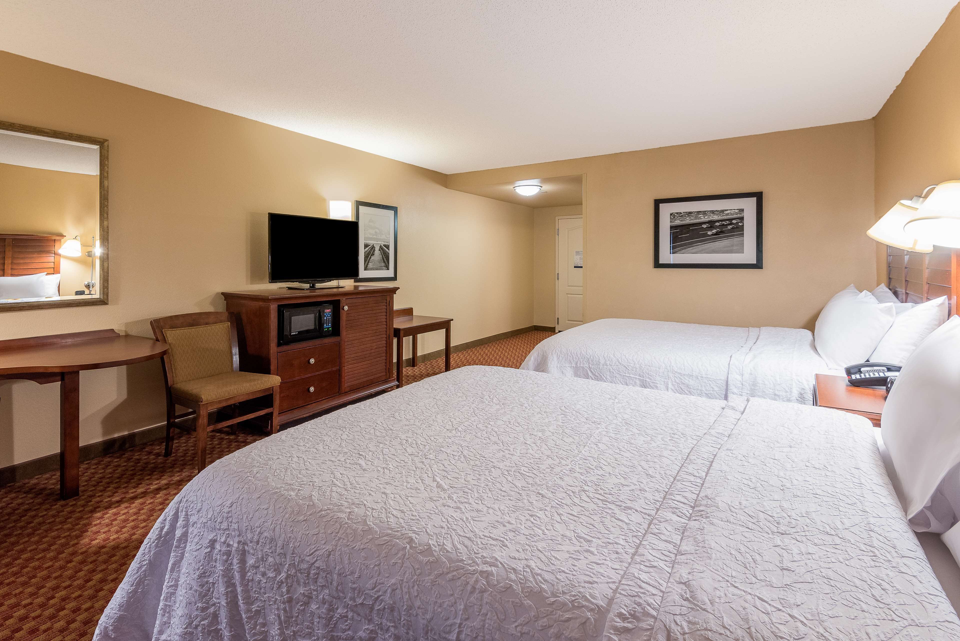 Une chambre d’hôtel avec deux lits, un bureau avec une télévision, une chaise et une commode.