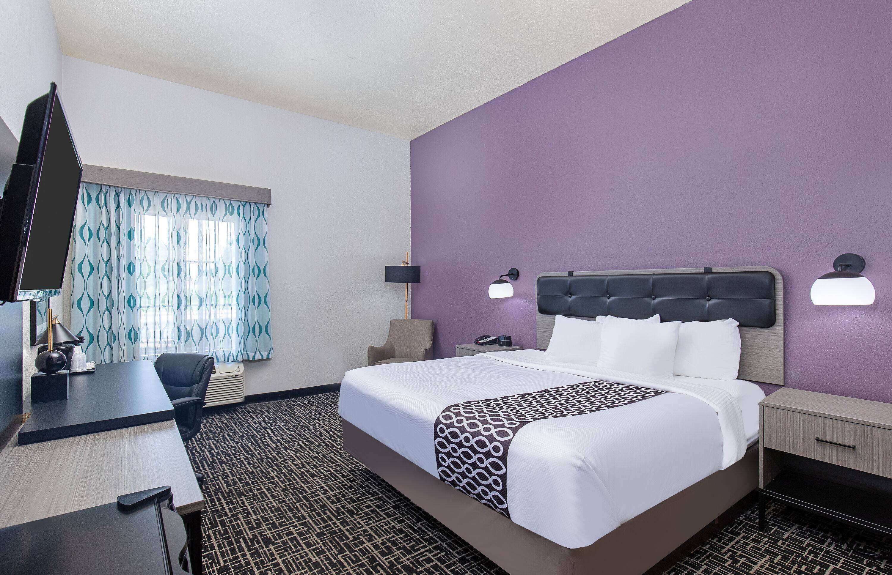 A hotel room with a bed, desk, chair, and a TV.
