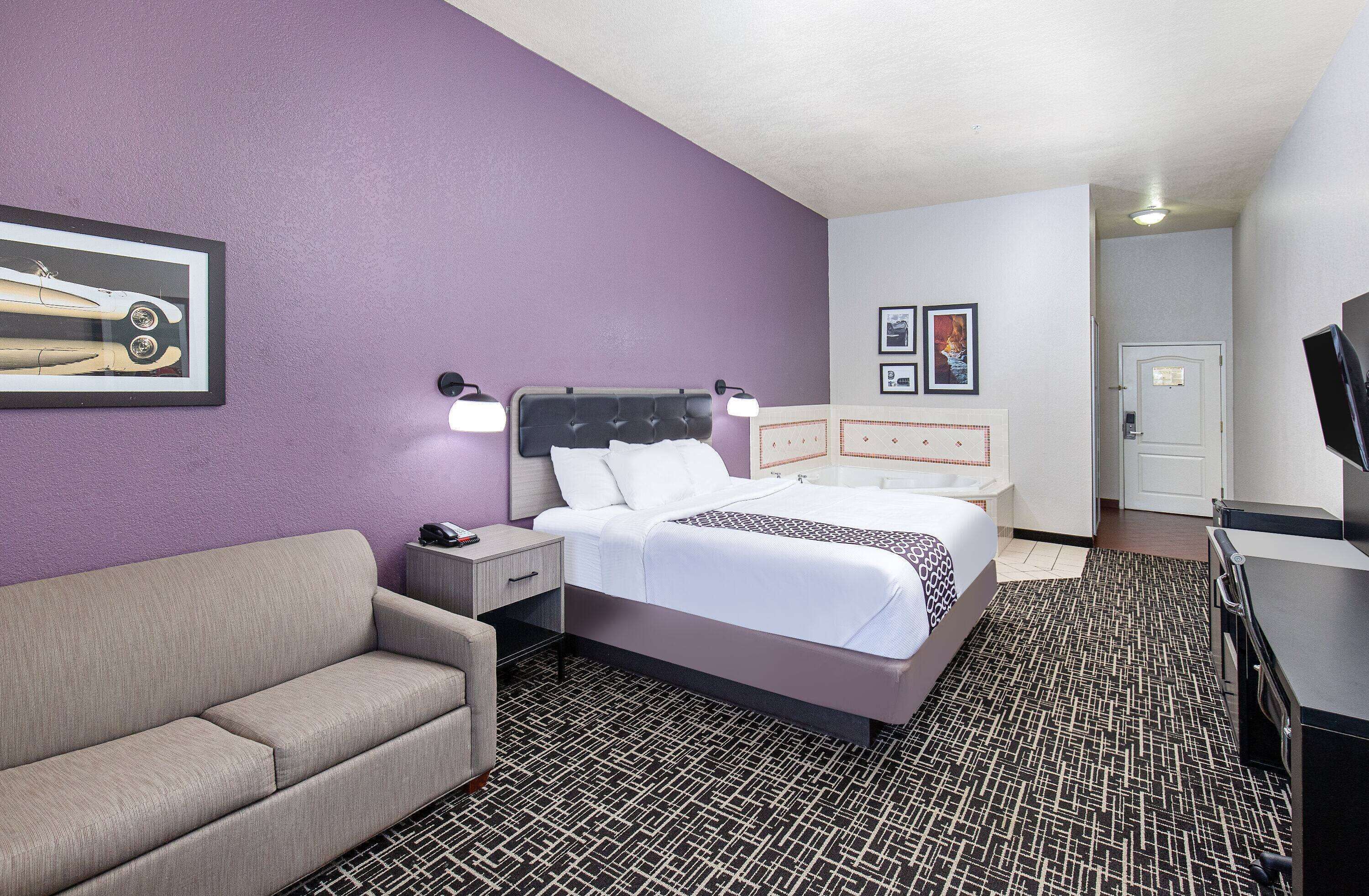 A hotel room with a bed, a nightstand, a sofa, a TV, and a door.