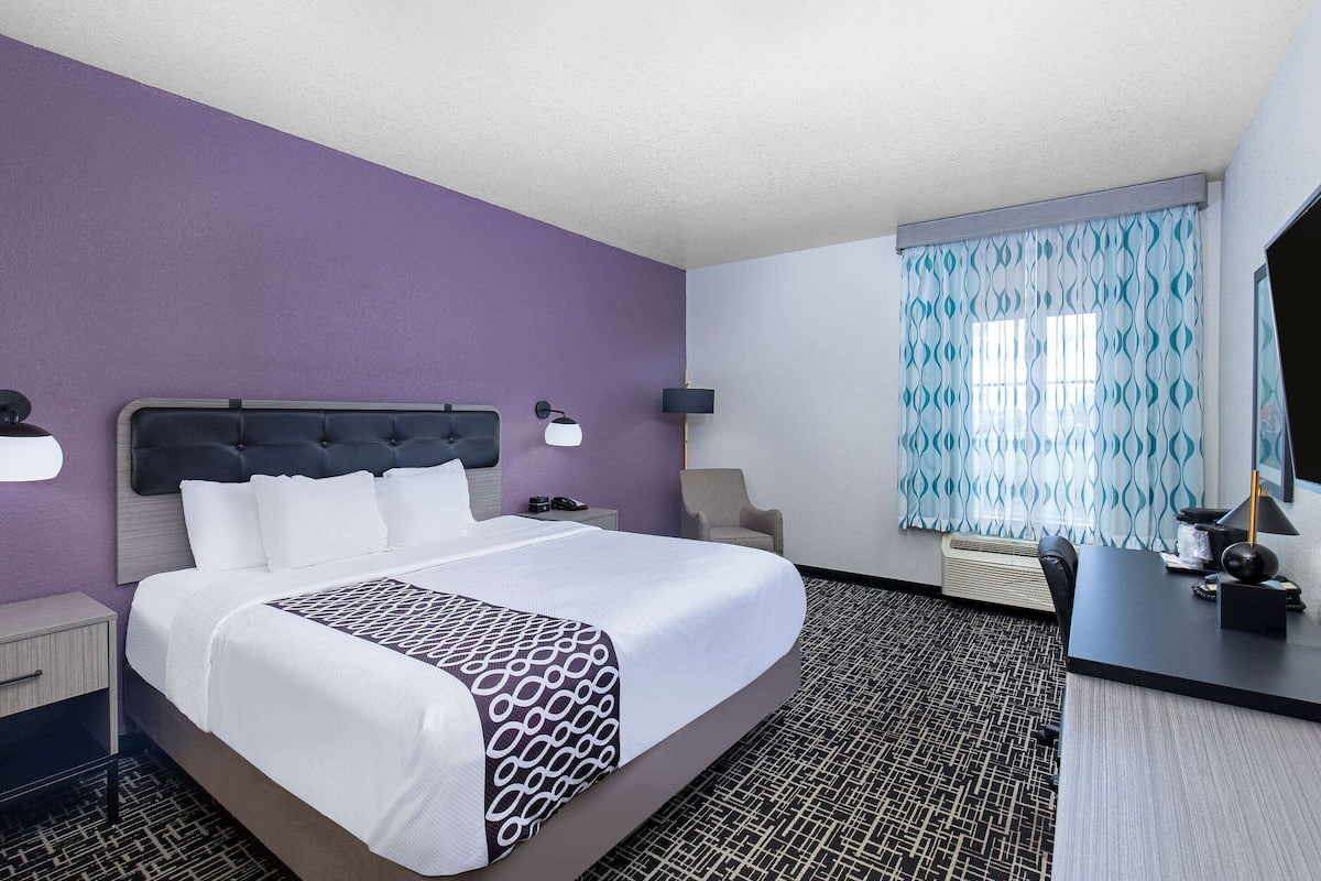 A hotel room with a bed, bedside tables, a desk, and a window with patterned curtains.