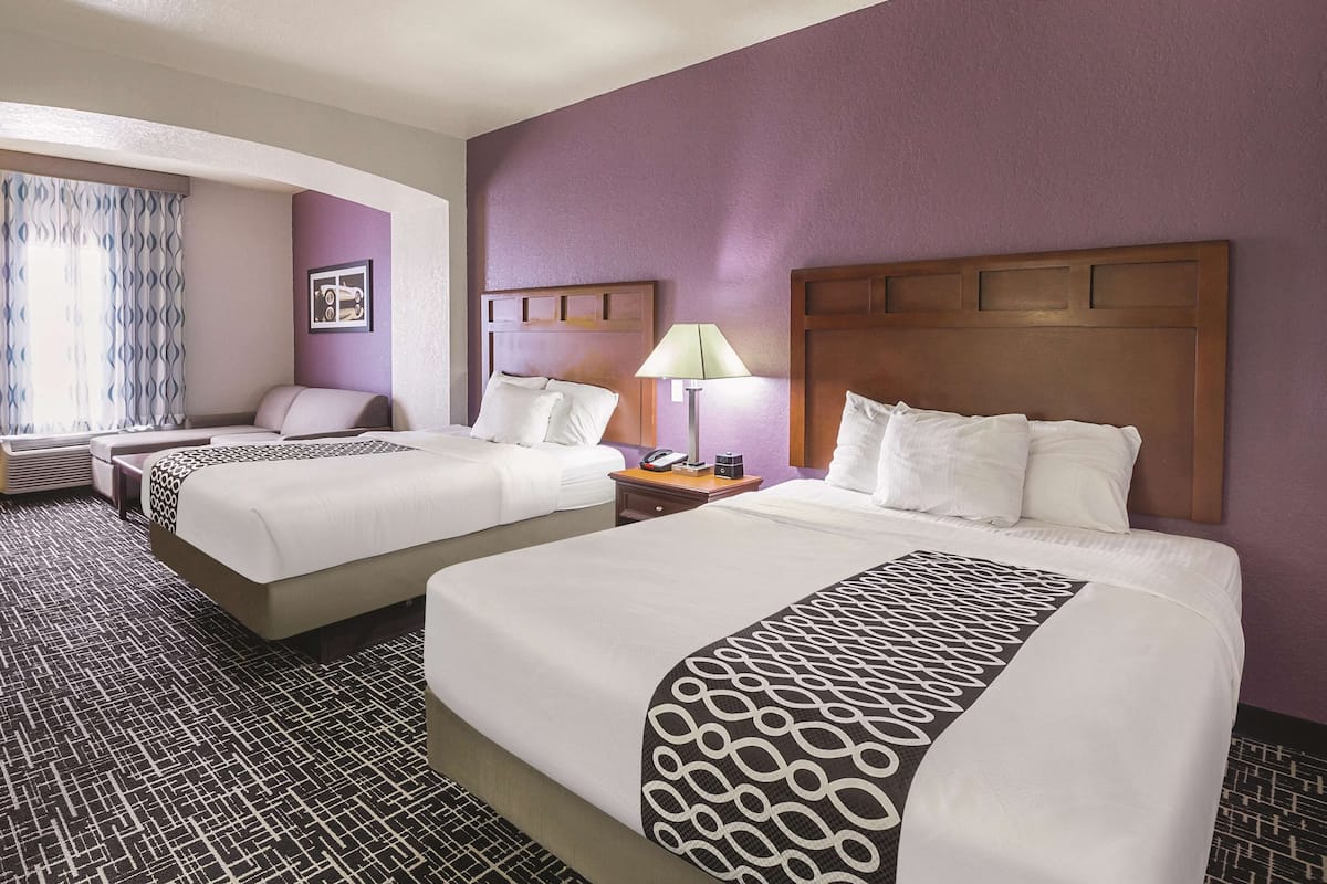 A hotel room with two beds, a sofa, a lamp, and a picture on the wall.