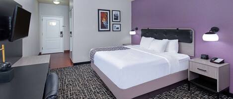 Ein Hotelzimmer mit Bett, Nachttisch, Lampe und Schreibtisch mit Stuhl.
