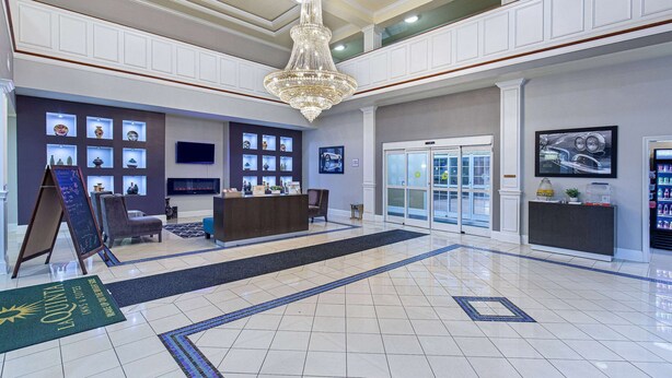 Een hotellobby met een receptiebalie, een kroonluchter, een groot raam en een muur met ingelijste foto's.