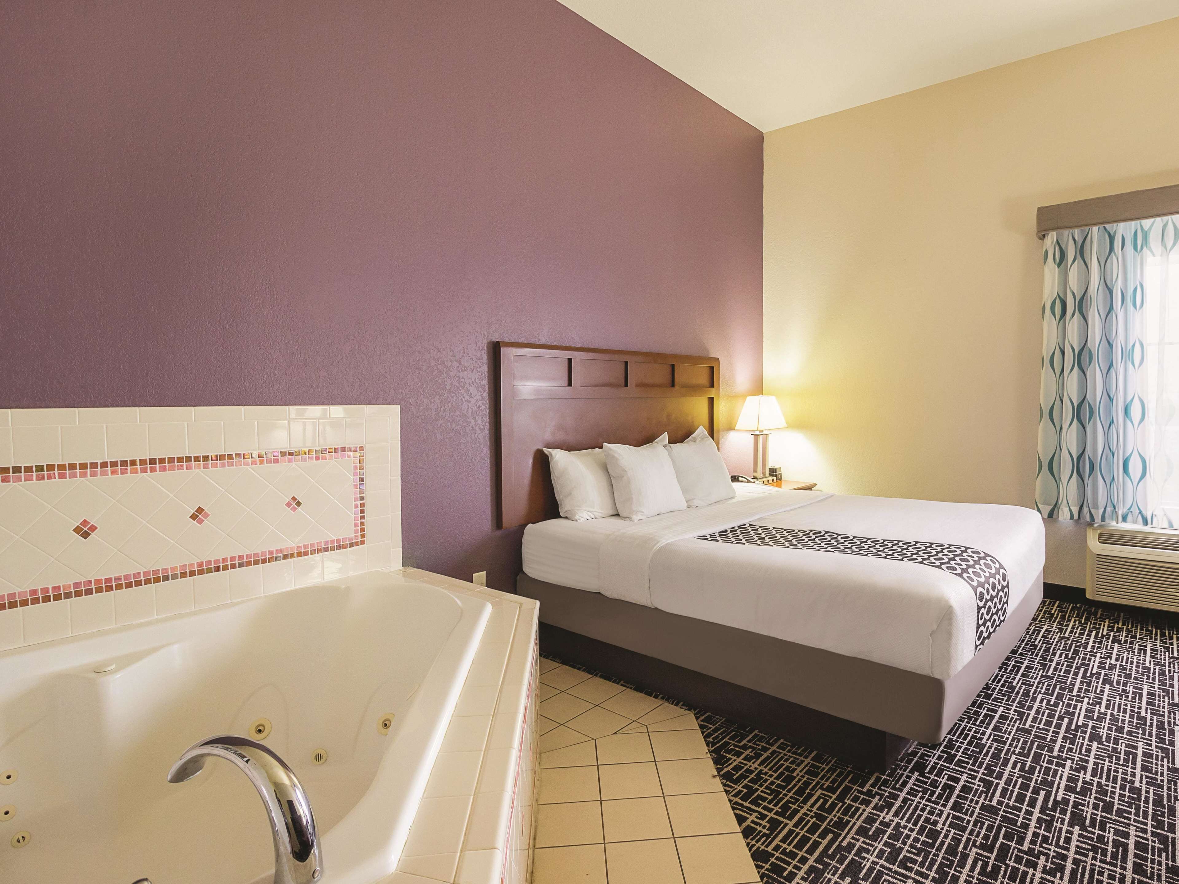 A hotel room with a large bed, a separate bathroom with a bathtub, and a window with patterned curtains.