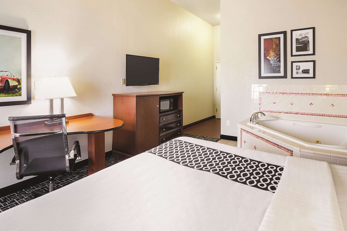 A hotel room with a bed, a desk, a chair, a television, a dresser, and a bathtub.