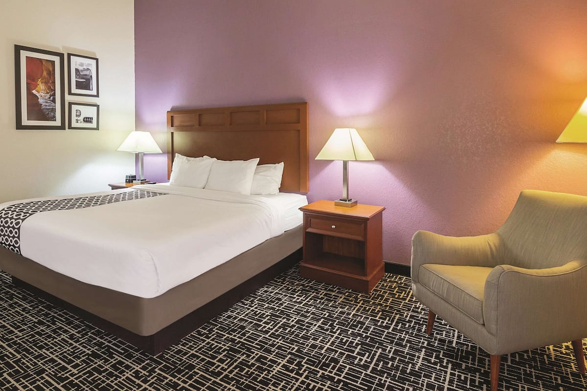 A hotel room with a large bed, two bedside lamps, a chair, and a patterned floor.
