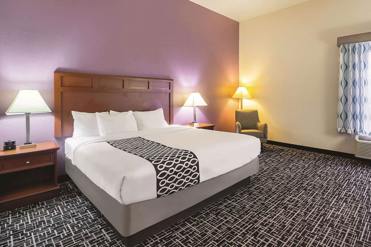A hotel room with a large bed, two bedside tables with lamps, a chair, and a patterned carpet.