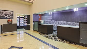 Een hotel receptie met betegelde vloer, receptiebalies, een koelkast en een televisie aan de muur.