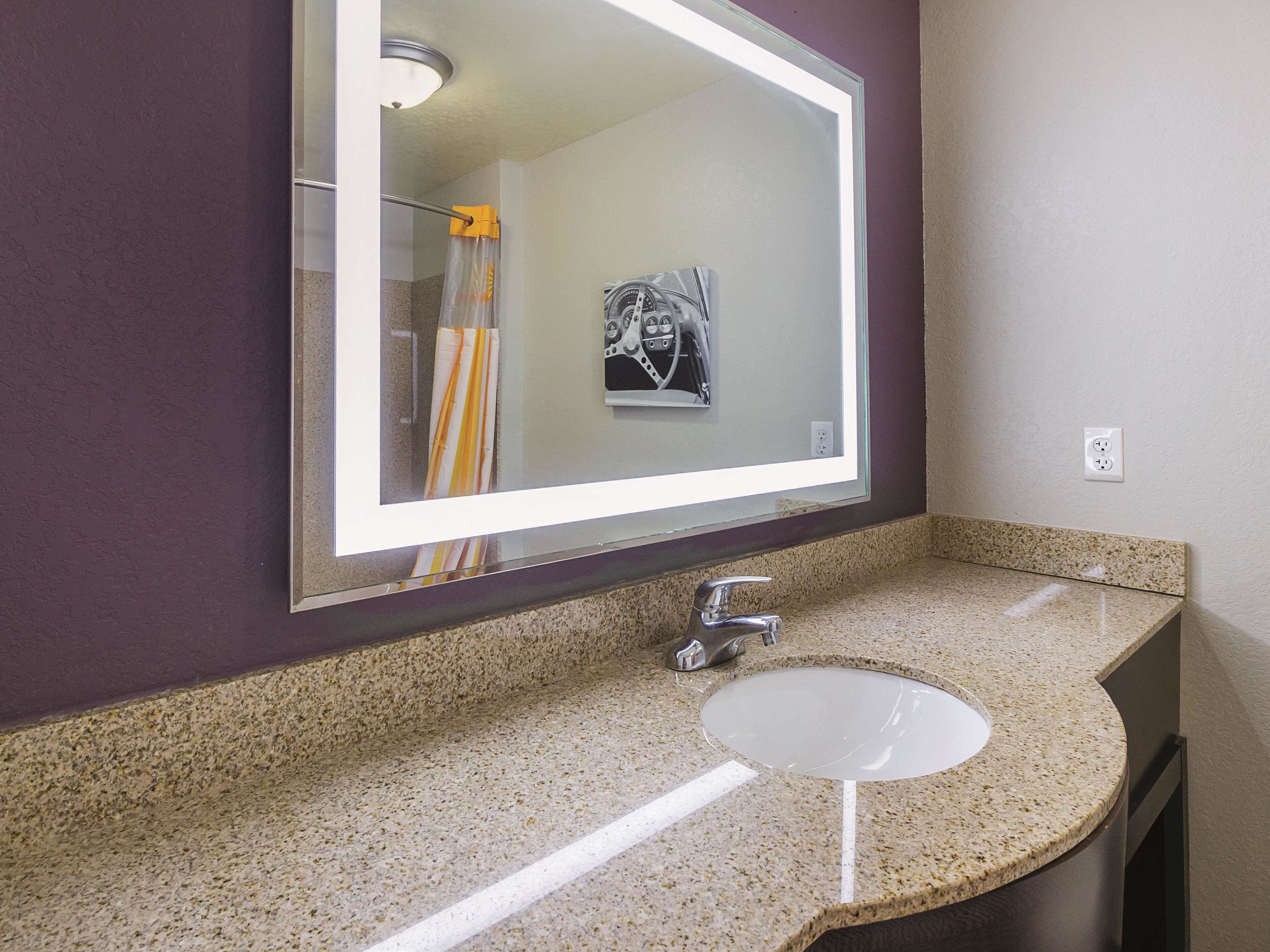 A bathroom with a granite countertop, a sink, a mirror, and a shower curtain.