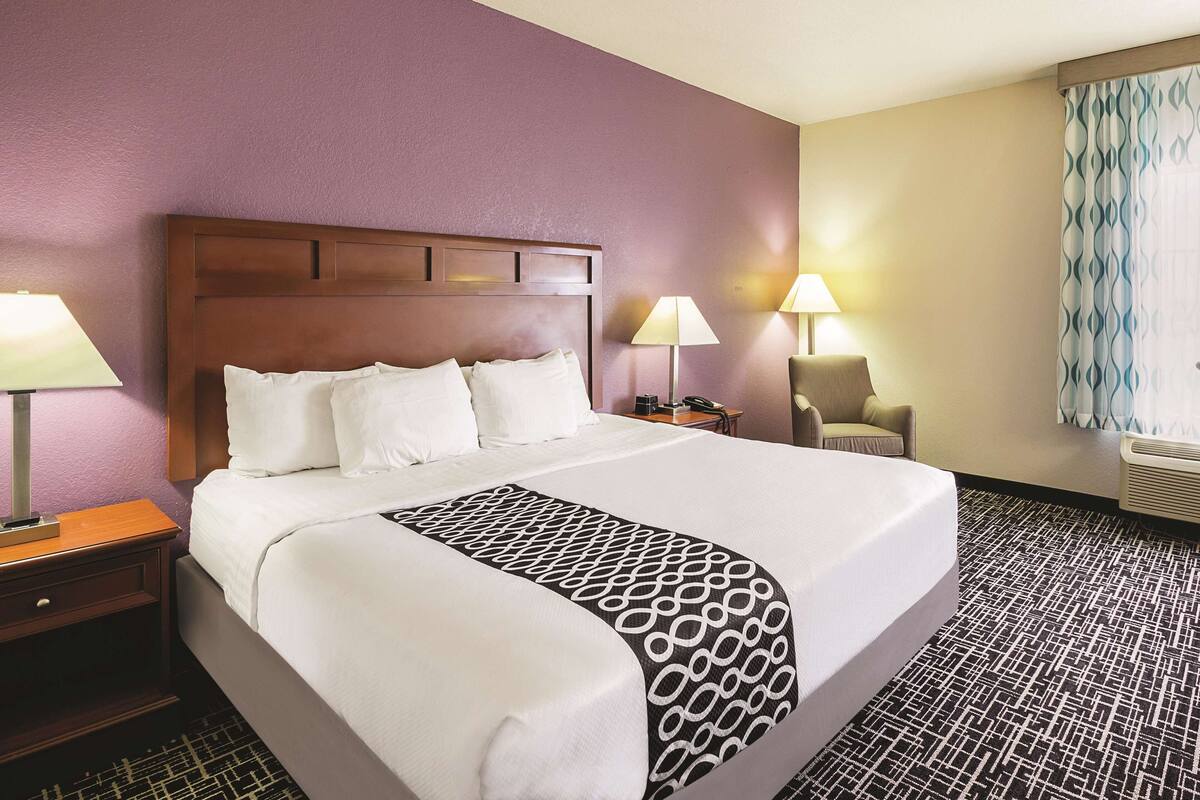 A hotel room with a large bed, two bedside lamps, a chair, and a desk with a telephone.