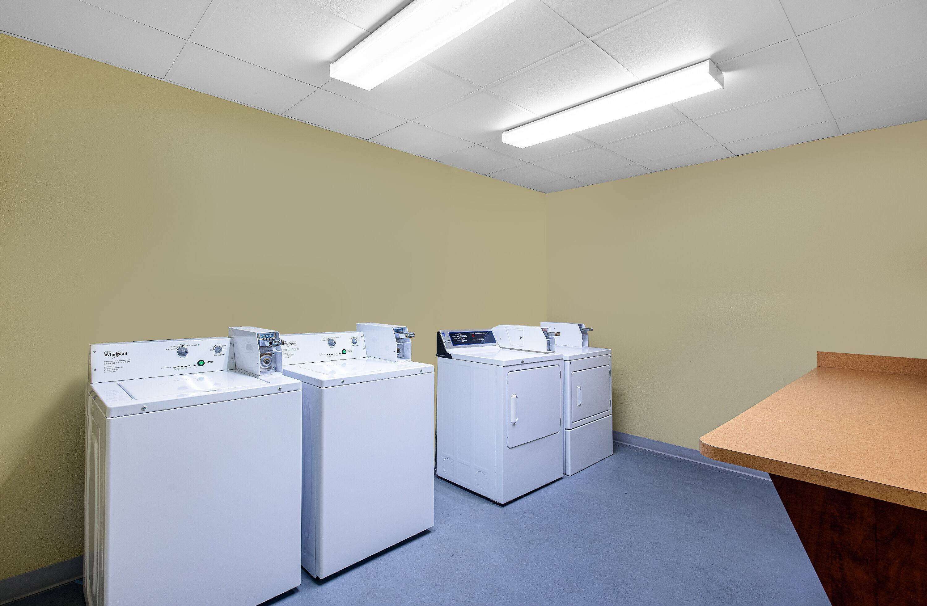 A laundry room with three Whirlpool washers and dryers, a wooden counter, and fluorescent ceiling lights.