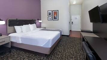 Una habitación de hotel con cama, mesita de noche, lámpara, televisor y una puerta que da a otra habitación.