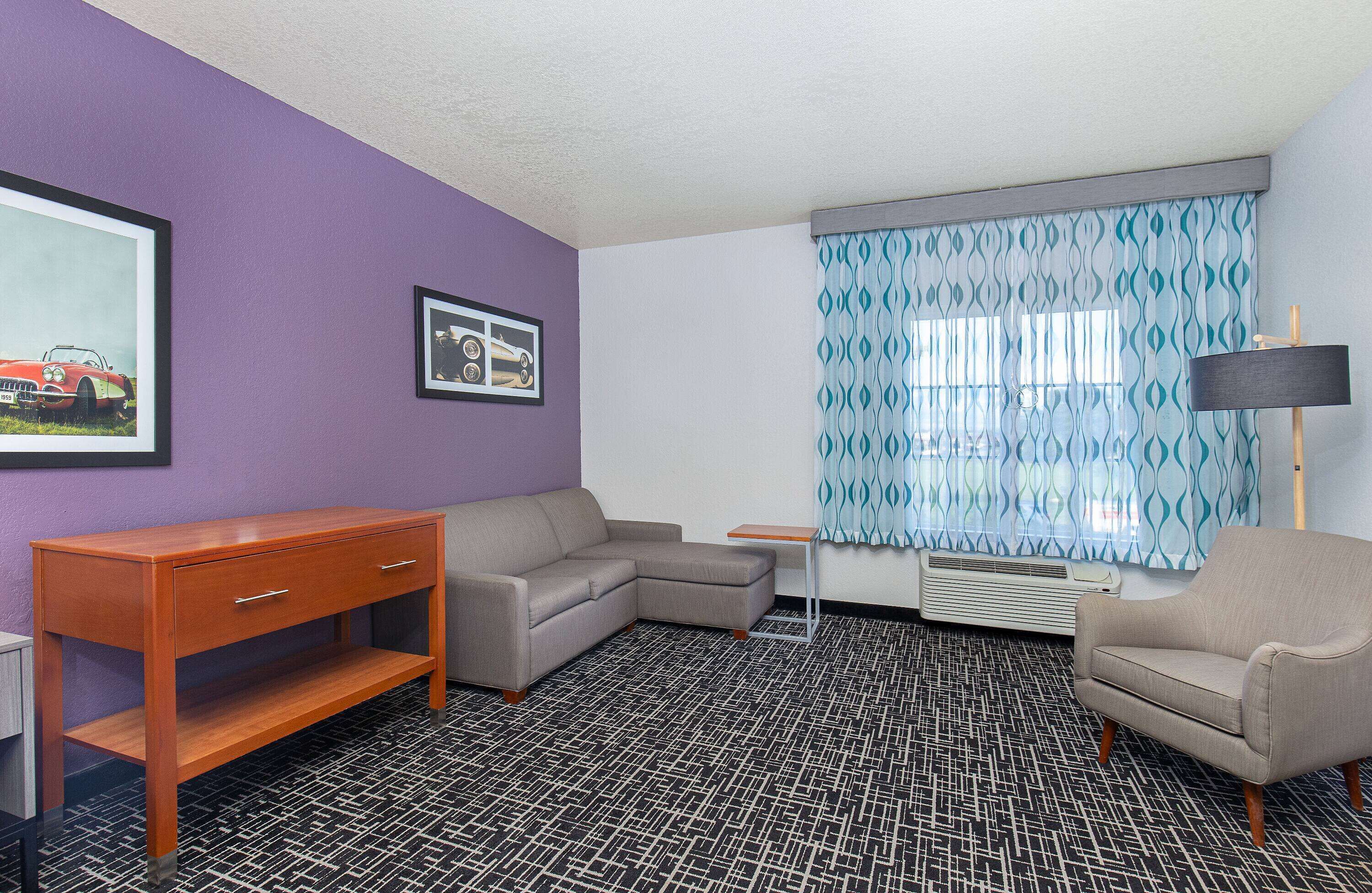A room with a sectional sofa, a wooden side table, a small table, and a lamp.