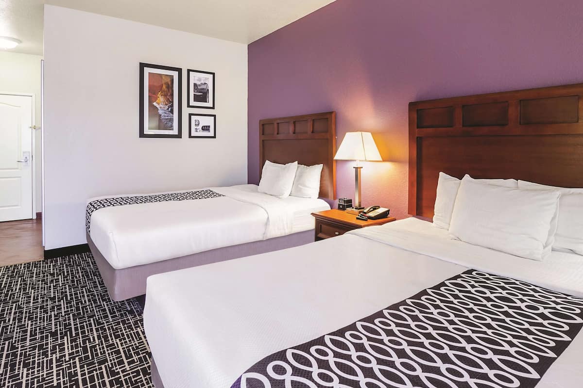 A hotel room with two beds, a nightstand with a lamp, and a wall with framed pictures.