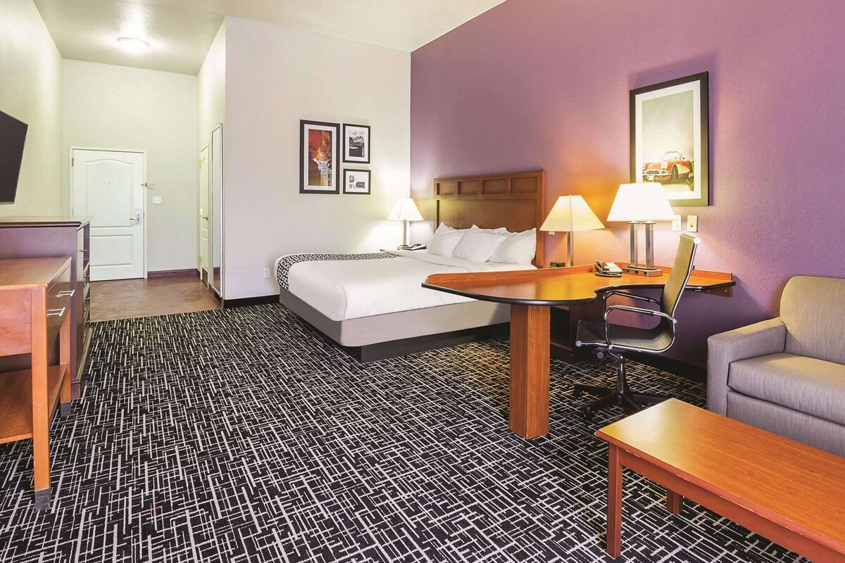 A hotel room with a bed, two bedside tables with lamps, a desk, a chair, and a sofa.