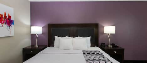 Habitación de hotel con una cama grande, dos mesitas de noche con lámparas, un cabecero y una pared con un cuadro abstracto y colorido.