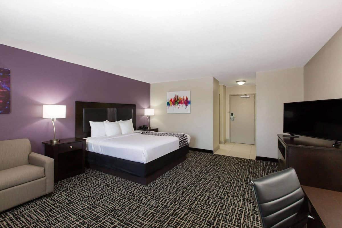 Una habitación de hotel con cama, escritorio, televisor, silla y puerta.