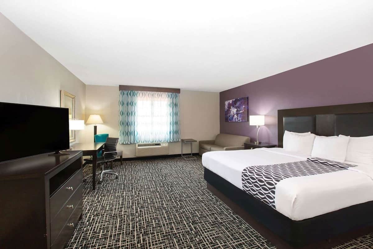 Habitación de hotel con una cama grande, televisión, escritorio con silla, sofá y ventana con cortinas.