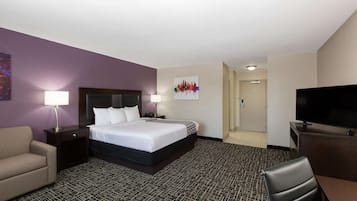 Una habitación de hotel con cama, escritorio, silla, televisión y mesita de noche con lámpara.