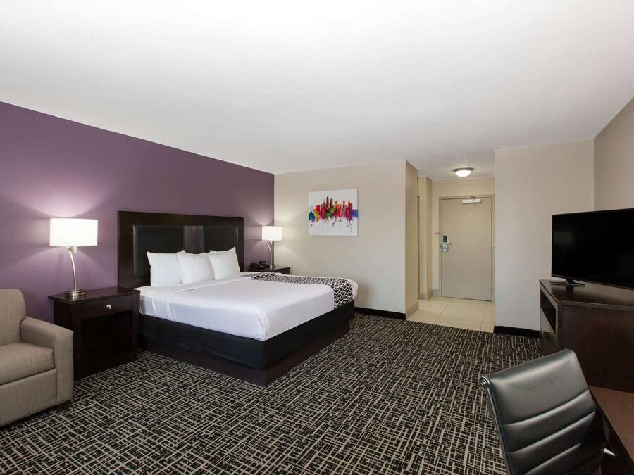 Una habitación de hotel con cama, escritorio, silla, televisión y mesita de noche con lámpara.