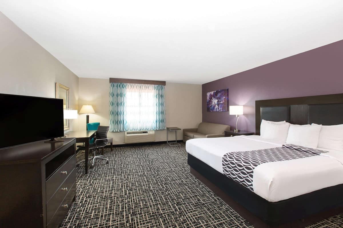 Una habitación de hotel con una cama grande, televisión, escritorio con silla, lámpara y ventana con cortinas.