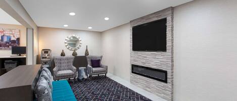 A modern living room with a sofa, armchairs, a coffee table, and a flat-screen TV mounted on a stone wall.