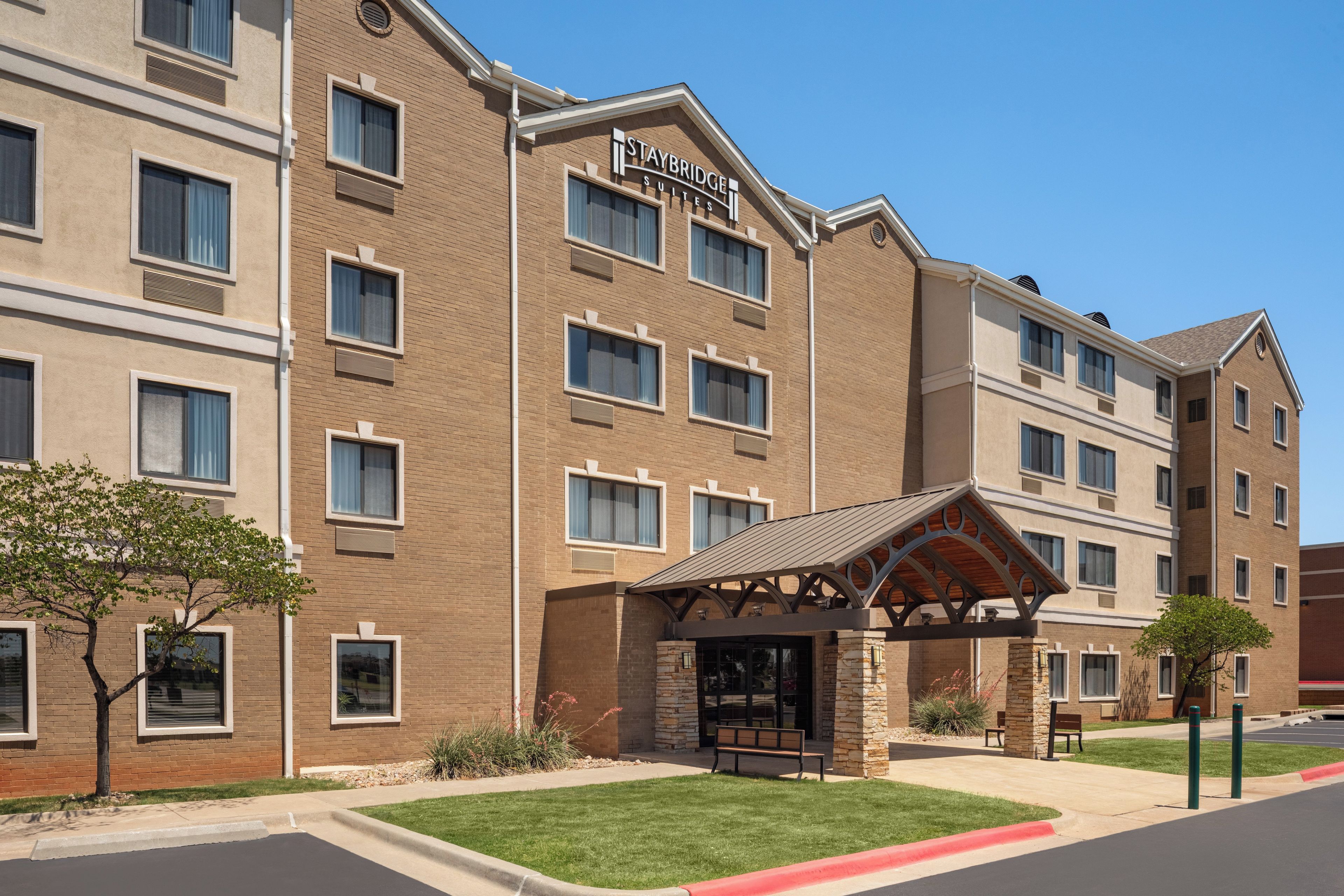 Un hotel Staybridge Suites con fachada de ladrillo, múltiples ventanales y una zona de entrada techada.