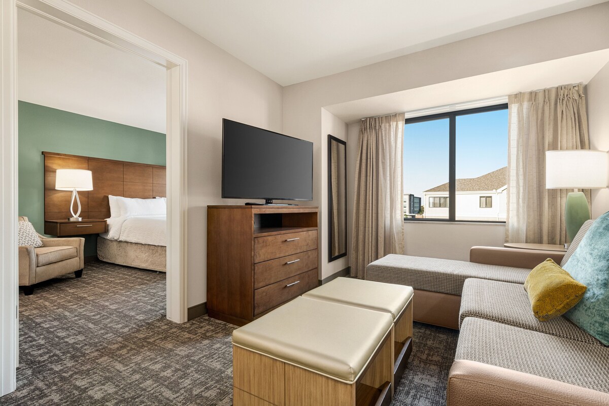 A hotel room with a bed, a TV, a desk, a sofa, and a window with curtains.