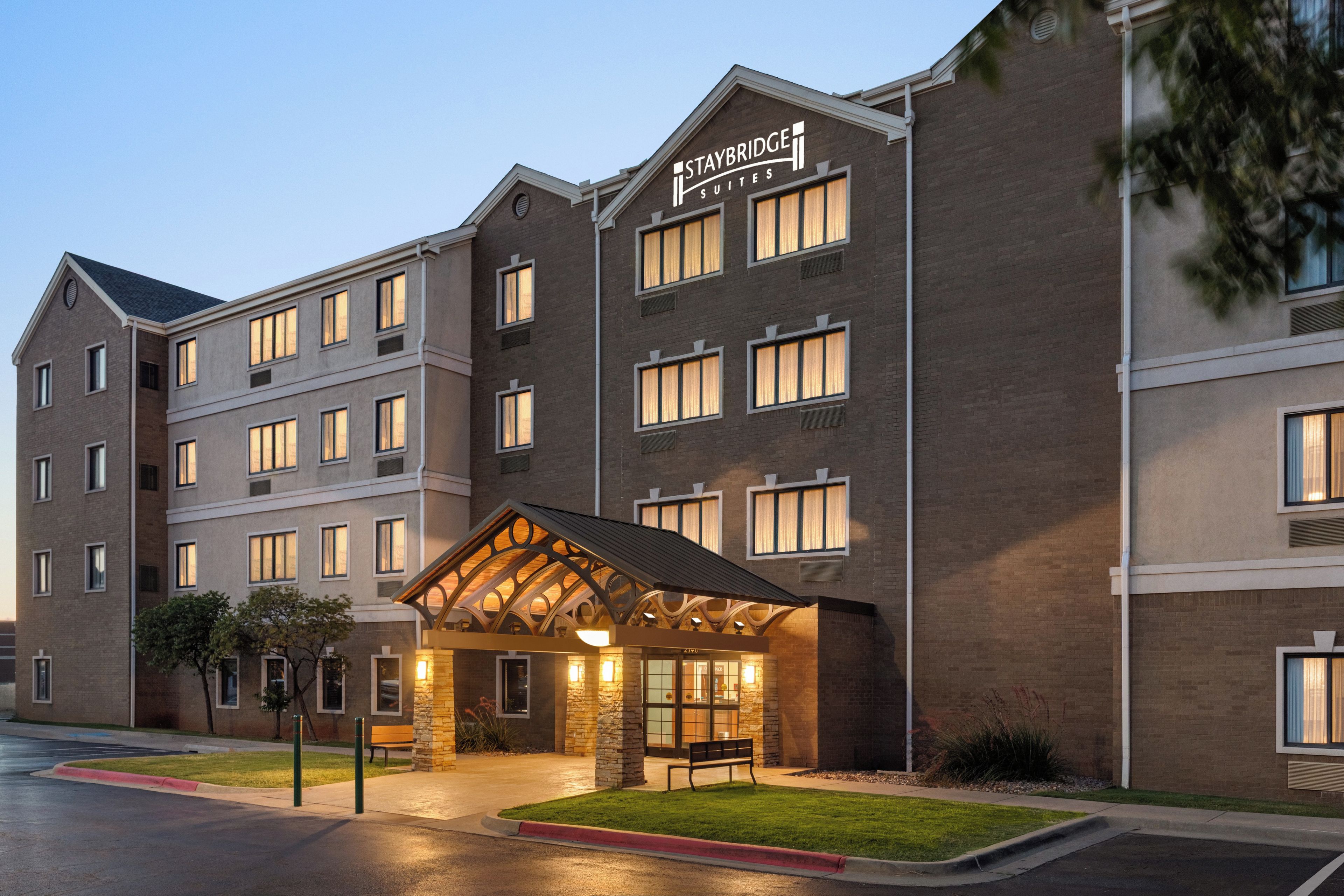A Staybridge Suites hotel with a brick facade, multiple windows, and a well-lit entrance.