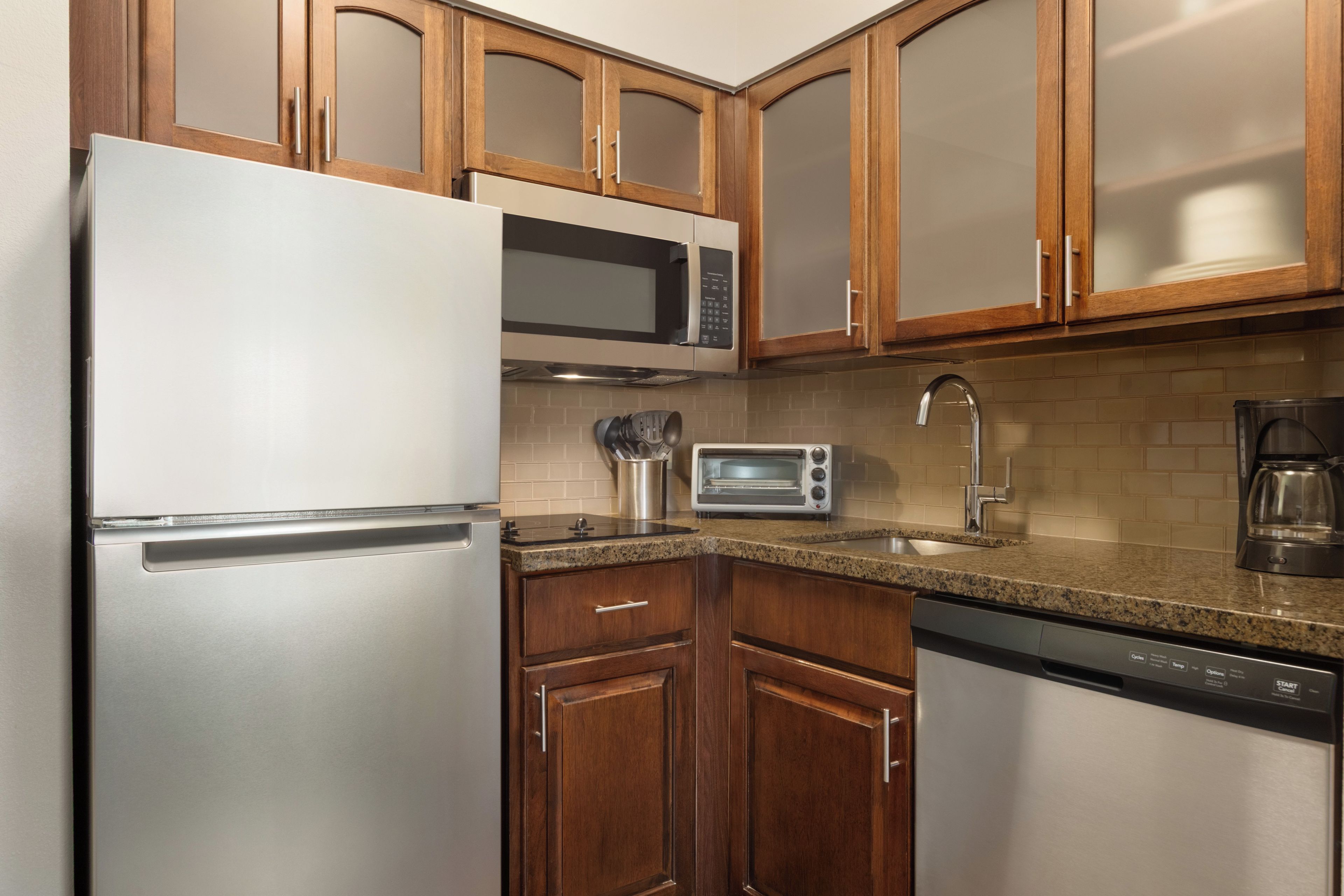 A kitchen with wooden cabinets, stainless steel appliances including a refrigerator, microwave, toaster, and dishwasher.