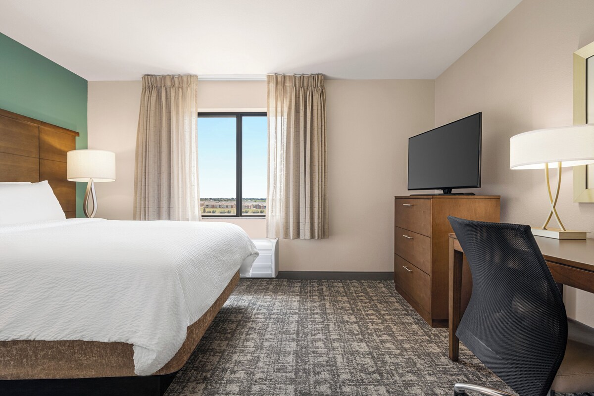 A hotel room with a bed, a desk, a television, and a view of the city.