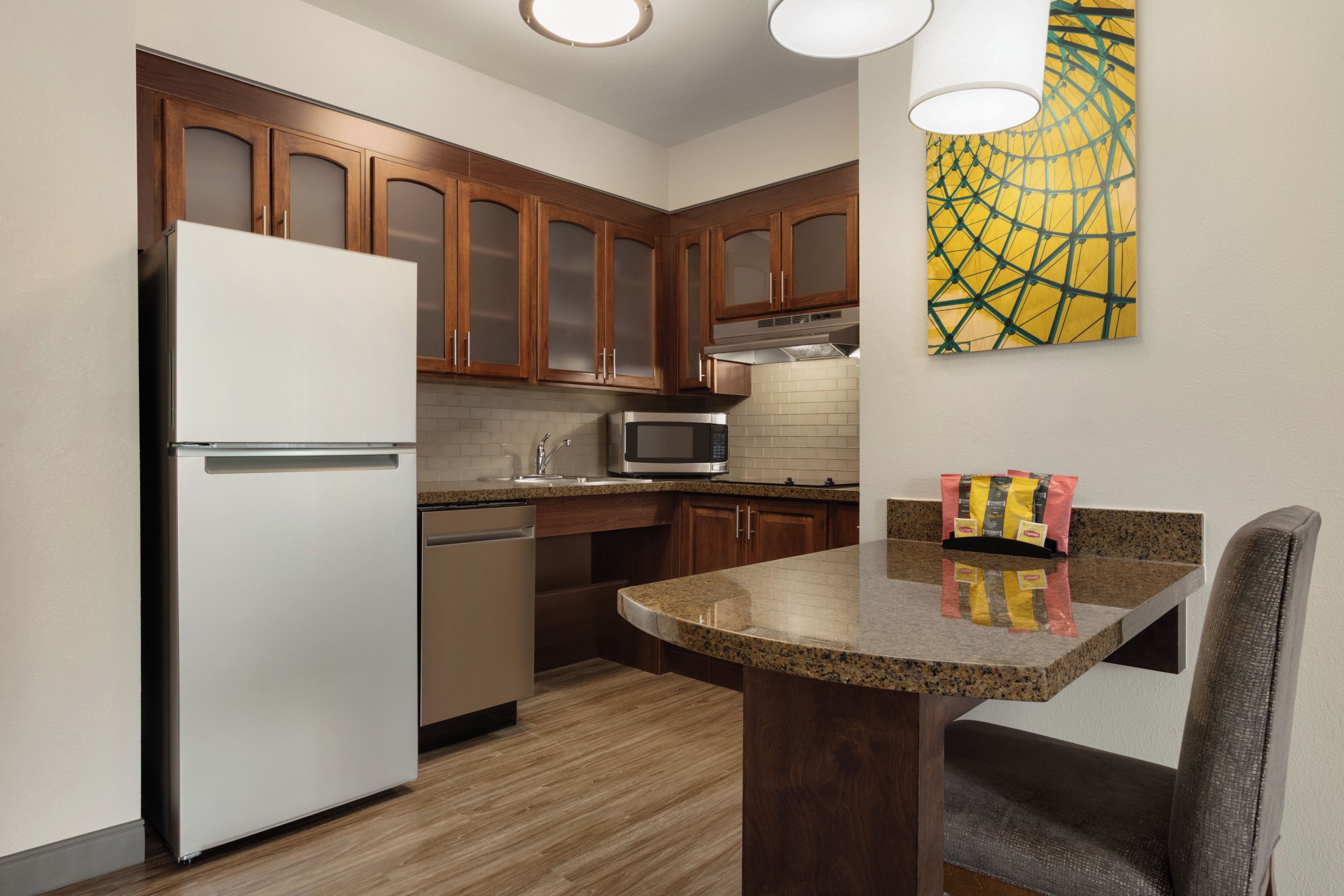 A modern kitchen with wooden cabinets, a stainless steel refrigerator, a microwave, and a granite countertop.