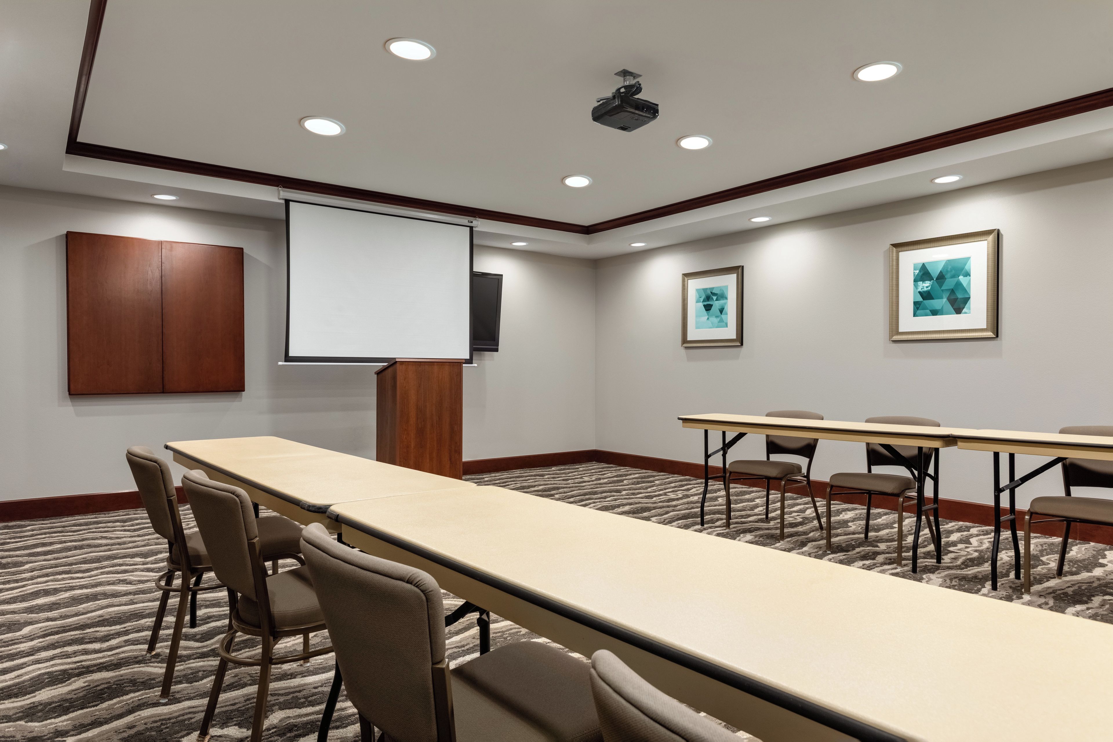 A conference room with a long table, chairs, a projector screen, and framed artwork on the walls.