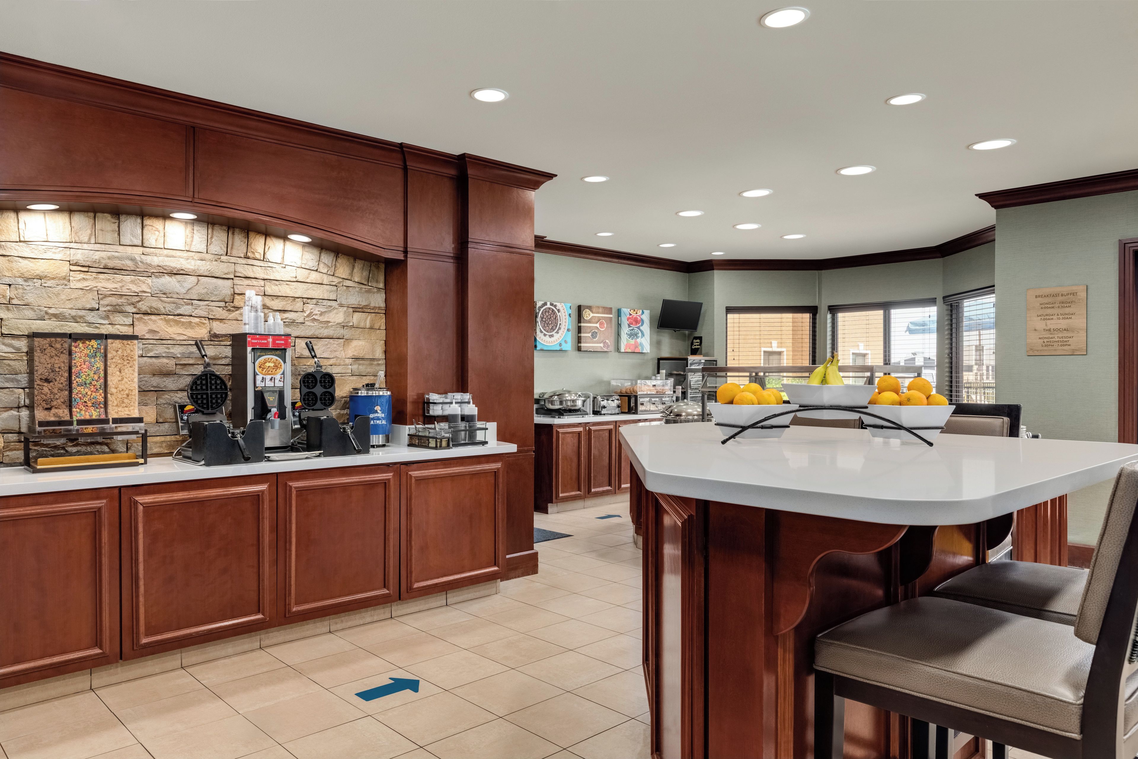 Zona de desayuno buffet con pared de piedra de fondo, estación de café y área de descanso con mesa y sillas.